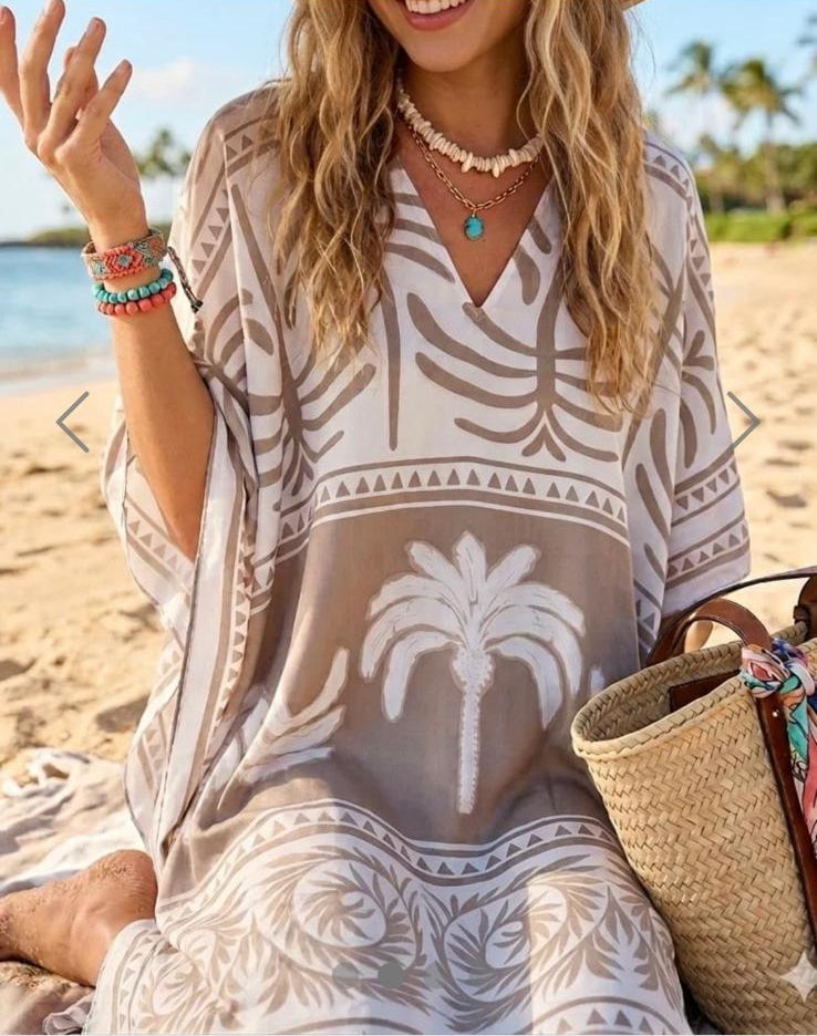 Woman in a palm tree print silk cover-up on a beach with NN Fashion Wholesale branding.